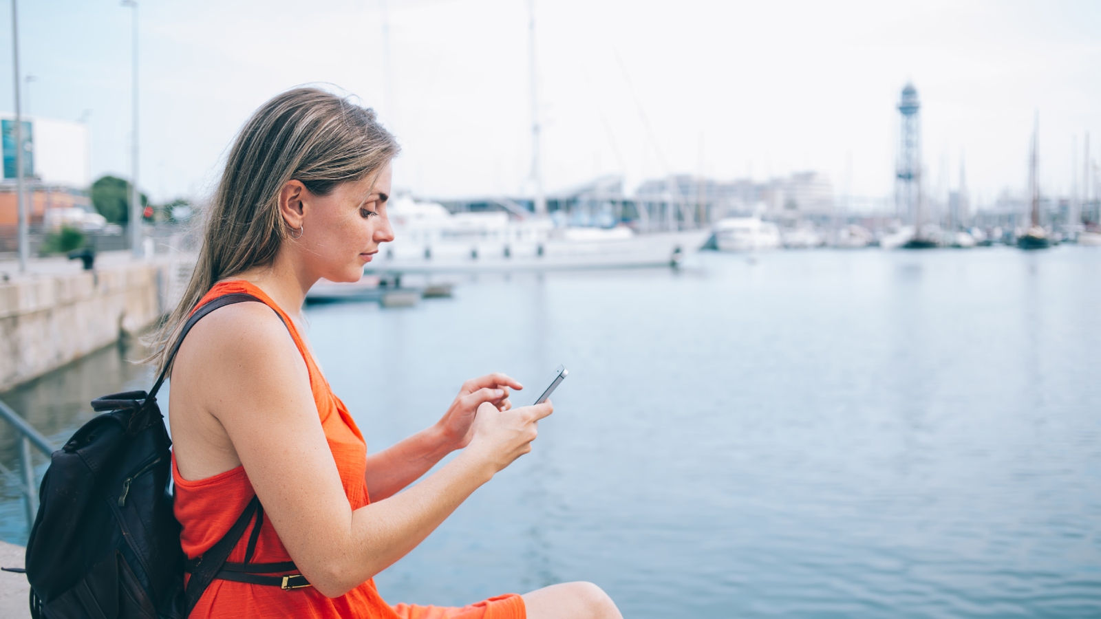 een vrouw is, zittend in een haventje, bezig op haar mobiele telefoon