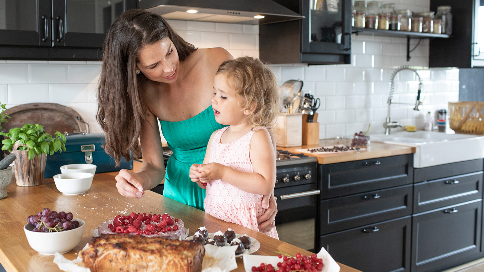 Sanne helpt haar dochtertje bij het versieren van een taart vol fruit