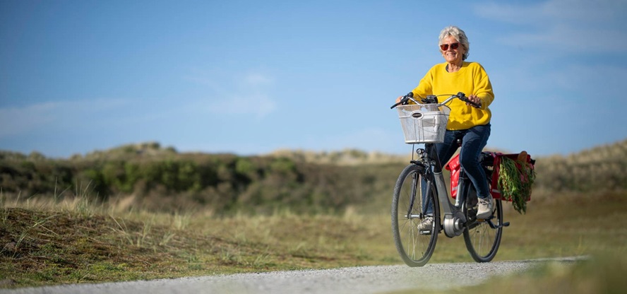een vrouw in een gele jas fietst op haar elektrische fiets over een duinpad
